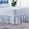 White embroidered ruffle bed skirt with black polka dots on a bed.