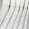 A close-up of white cotton embroidered lace trim in various patterns and widths laid out on a surface.