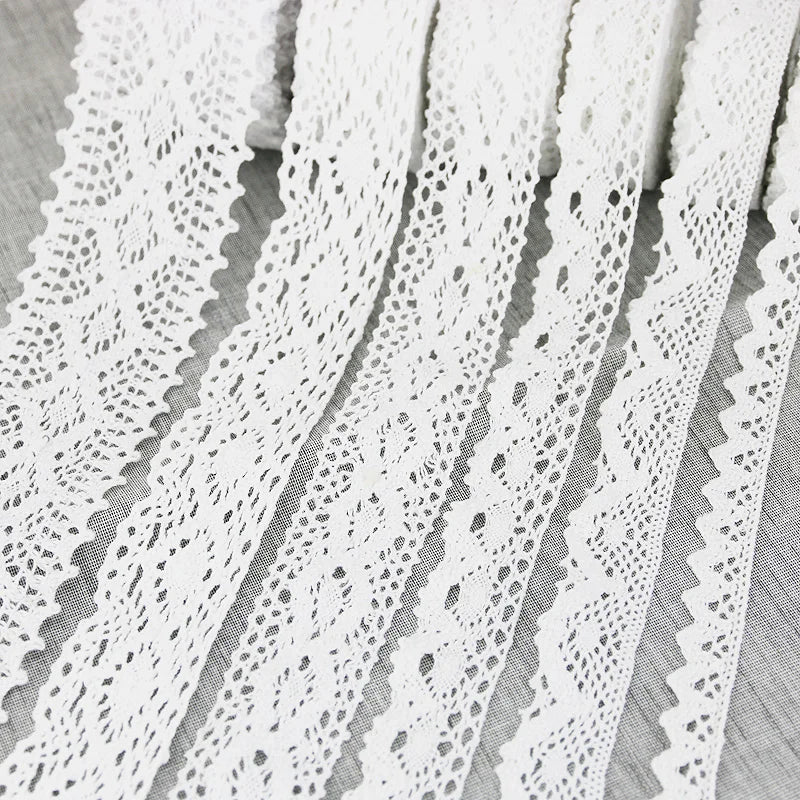 A close-up of white cotton embroidered lace trim in various patterns and widths laid out on a surface.
