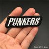 A hand holds a black embroidered punk badge with the word PUNKERS stitched in white thread.