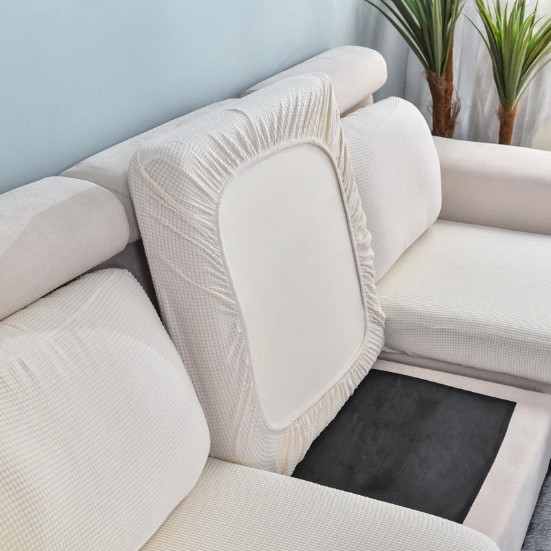 A white stretch sofa seat cushion protector slipcover with a padded cover and a dark mat on a light-colored sofa.