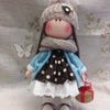 A handmade cotton toy filler batting doll dressed in a gray knitted hat and blue clothing.
