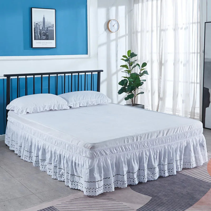 A white bed with an embroidered ruffle skirt is shown in a bright room.