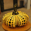 A yellow pumpkin plush cushion covered in black polka dots.