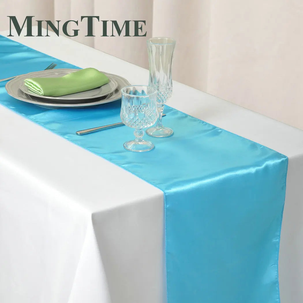 Elegant satin blue table runner with a green napkin and glassware on a white tablecloth