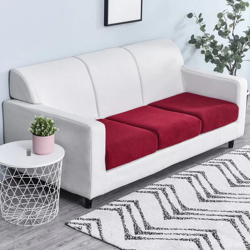 A white sofa with a red seat cushion cover and a white patterned rug.