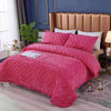A pink crystal velvet quilted bedspread is displayed on a bed with a gold upholstered headboard.