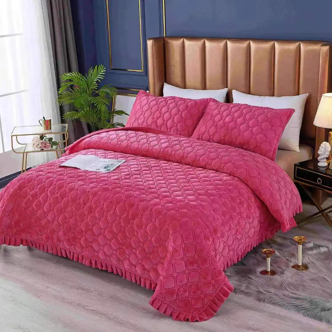 A pink crystal velvet quilted bedspread is displayed on a bed with a gold upholstered headboard.