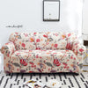 A floral patterned stretch elastic sofa cover in cream and pink tones displayed on a white rug.