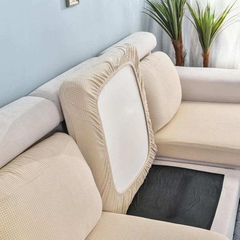 A beige stretch sofa seat cushion protector slipcover is shown on a light blue wall with potted greenery.