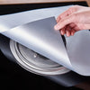 A hand is holding a sheet of reusable non-stick gas stove cleaning mat, showing its texture and thickness.