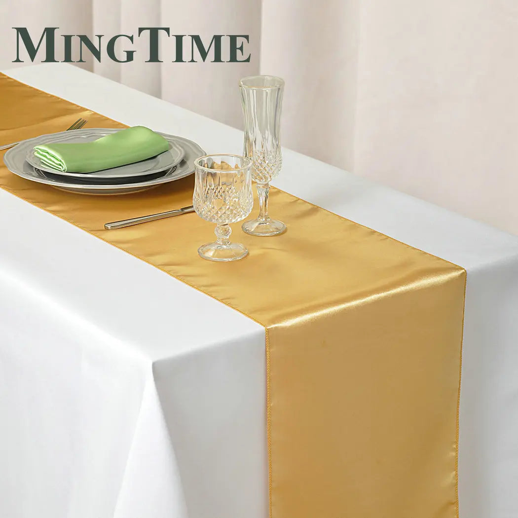 Elegant gold satin table runner displayed on a white tablecloth with glassware and cutlery.