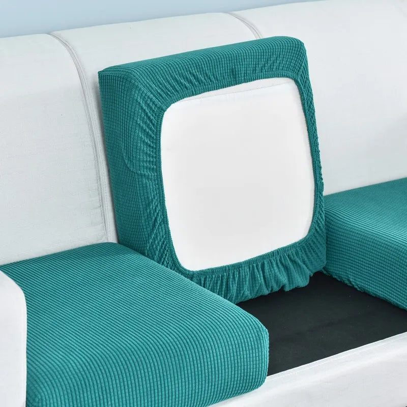 A teal stretch sofa seat cushion protector slipcover with a white inner cushion shown on a white sofa.