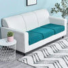 A white stretch sofa with teal seat cushions and a patterned rug in a bright room.