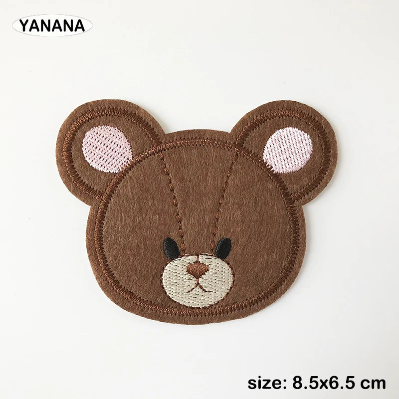 A brown felt animal patch of a bear face with pink ears and embroidered features.
