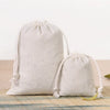 A set of natural beige cotton drawstring gift bags lying on a wooden surface.