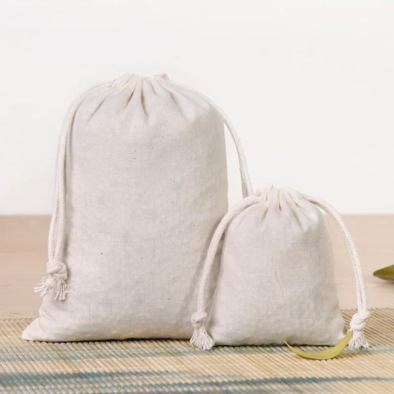 A set of natural beige cotton drawstring gift bags lying on a wooden surface.
