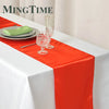 Elegant satin orange table runner displayed on a white tablecloth with glassware and a green napkin.