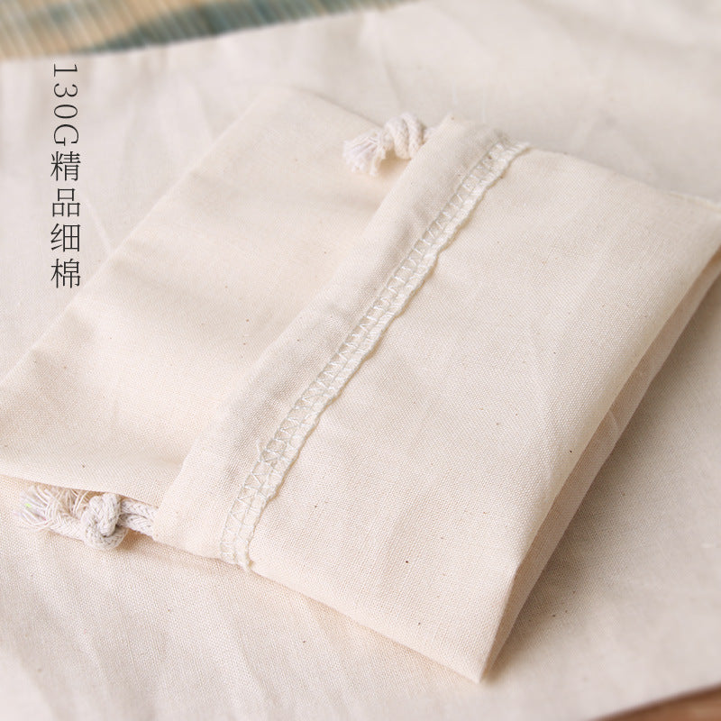 A close-up of a natural cotton drawstring gift bag in beige fabric resting on a light background.
