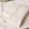 A close-up of a natural cotton drawstring gift bag in off-white fabric with visible stitching and tassels.