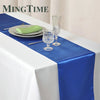 A blue satin table runner is displayed on a white tablecloth with silverware and glassware.