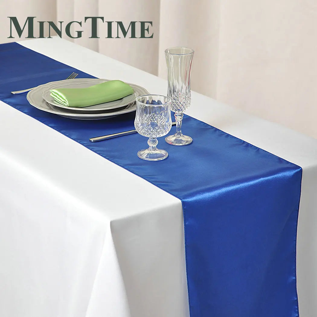 A blue satin table runner is displayed on a white tablecloth with silverware and glassware.