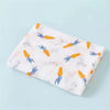 A folded white cotton muslin swaddle blanket with a pattern of orange and blue carrots.