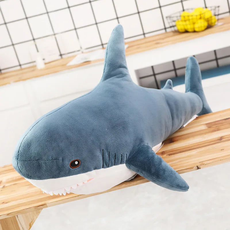 A soft blue and white giant shark plush toy lying on a wooden surface.
