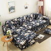 A dark floral patterned L-shaped sofa protector cover displayed on a light wood floor.