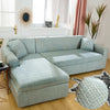 A light blue L-shaped sofa protector cover placed on a wooden floor in a bright room.