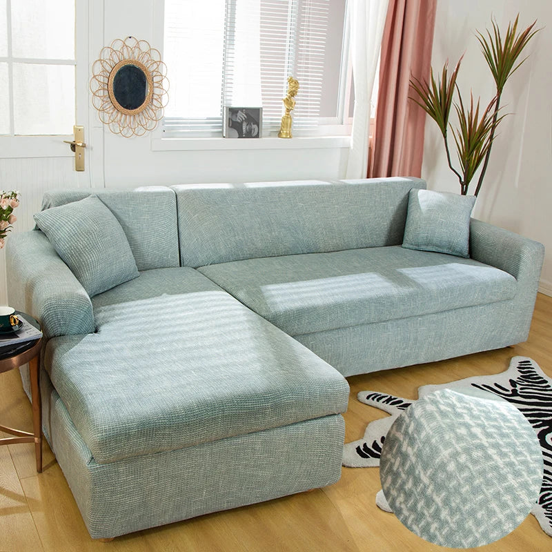 A light blue L-shaped sofa protector cover placed on a wooden floor in a bright room.