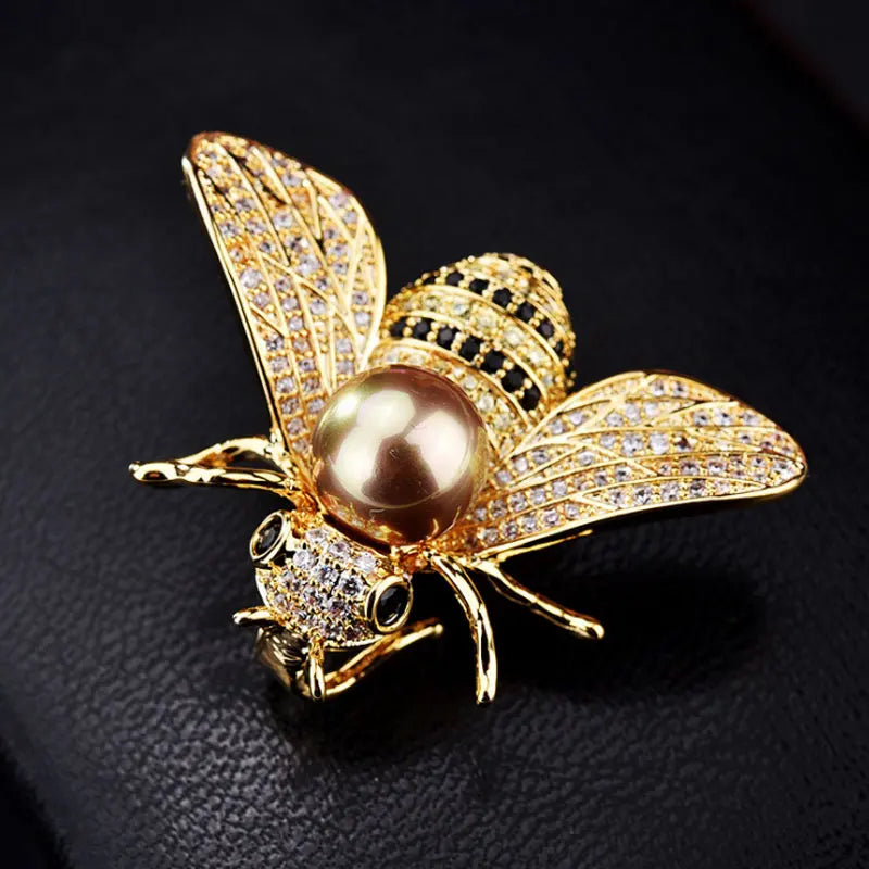 A gold and diamond crystal bee brooch featuring a pearl accent on the body and wings.