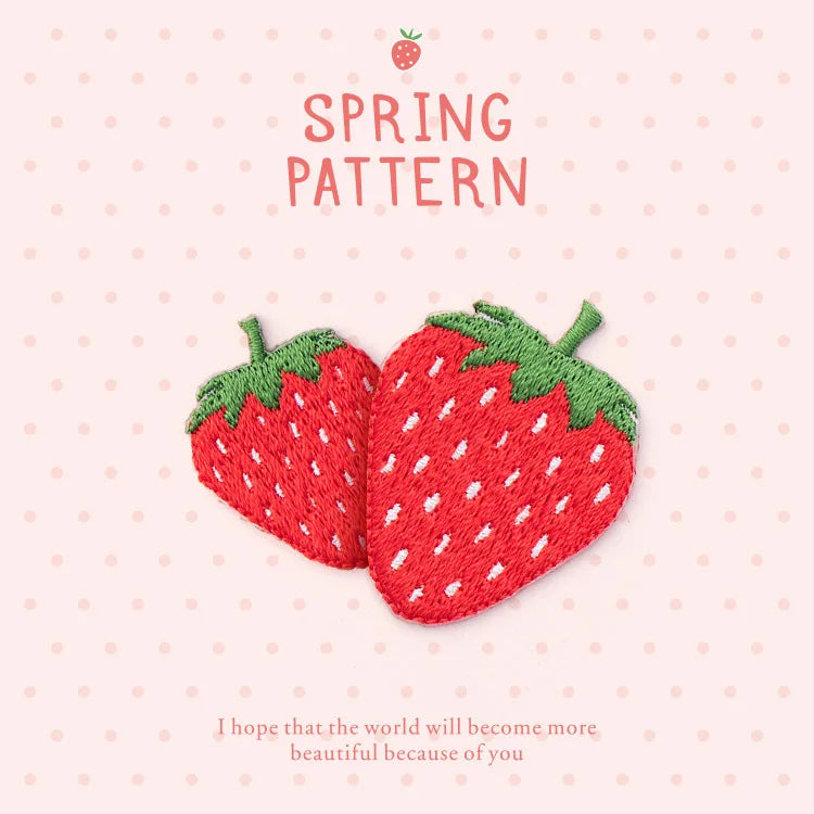 A red strawberry embroidery patch with green leaves and stems on a light pink background.
