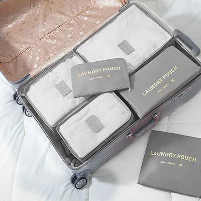 A silver suitcase is open, containing a pink fabric bag and several grey laundry pouches with white cloths.