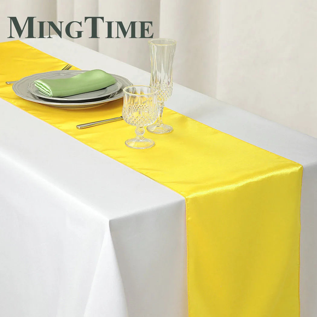 Elegant yellow satin table runner displayed on a white tablecloth with silverware and glassware.