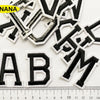 A collection of black and white alphabet letter embroidery patches scattered on a white background.