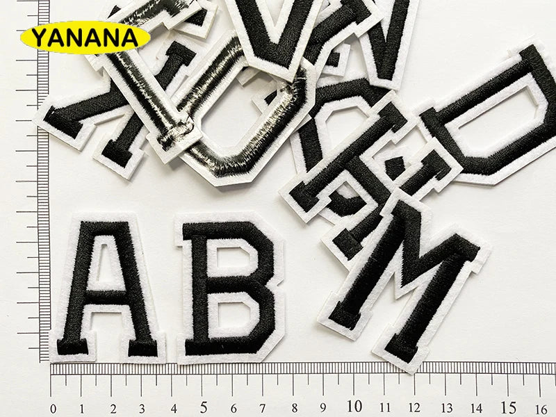 A collection of black and white alphabet letter embroidery patches scattered on a white background.