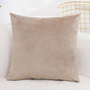 A square, beige velvet decorative cushion cover resting on a white surface next to a gold wire chair.