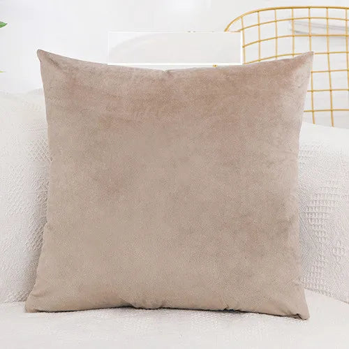 A square, beige velvet decorative cushion cover resting on a white surface next to a gold wire chair.