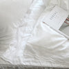 A luxury white ruffle duvet cover is displayed on a bed, with a box of cereal visible nearby.