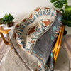 A bohemian geometric throw blanket featuring earthy tones and patterned designs draped over a wooden chair.