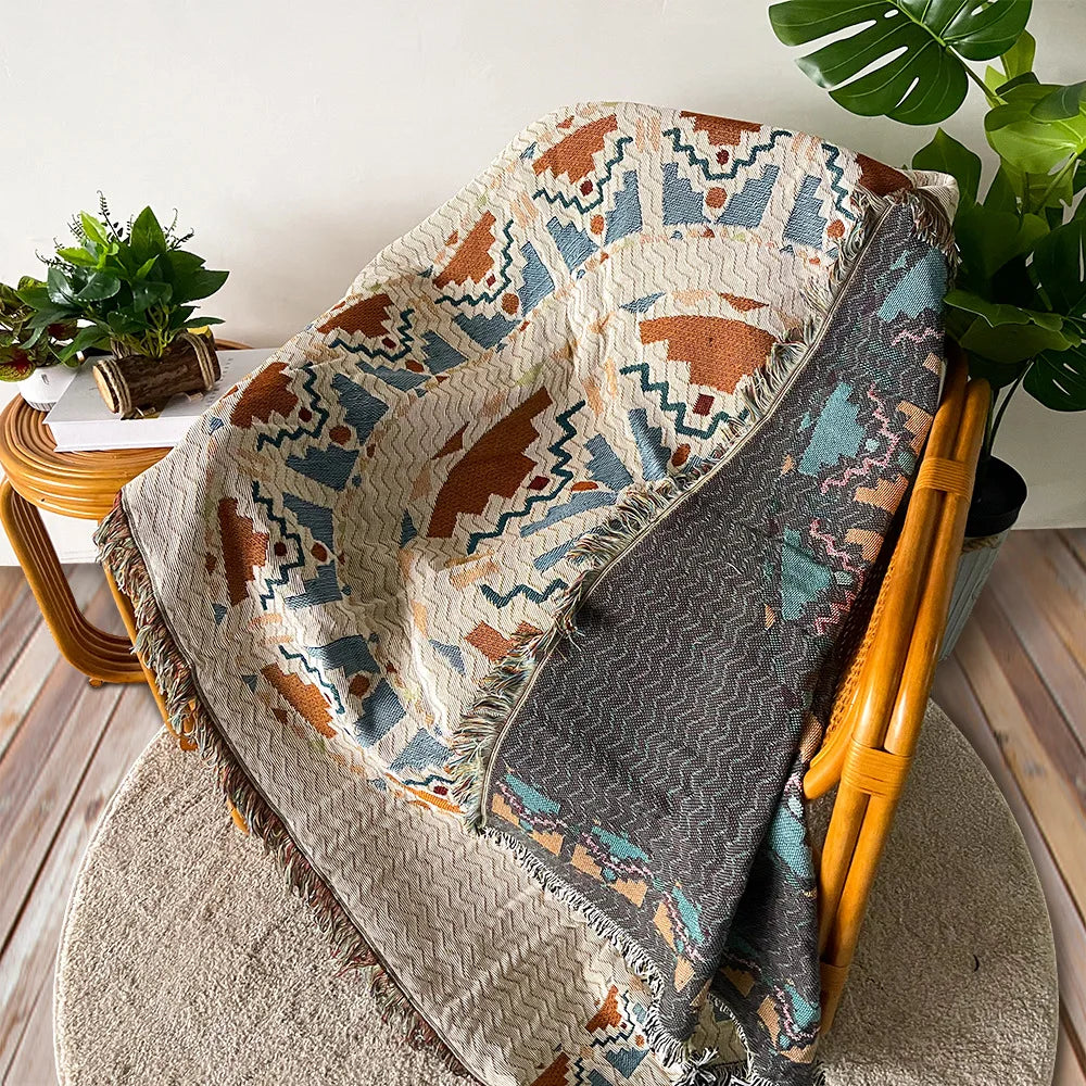 A bohemian geometric throw blanket featuring earthy tones and patterned designs draped over a wooden chair.