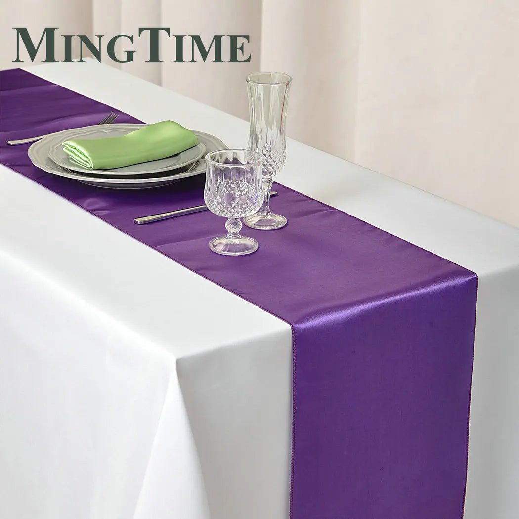 Elegant purple satin table runner displayed on a white tablecloth with silverware and glassware.