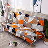 A sofa bed covered in a geometric print spandex slipcover featuring shades of orange, gray, white, and navy.