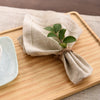 A bundle of natural linen fabric tied with twine, resting on a wooden board next to a light blue ceramic plate.