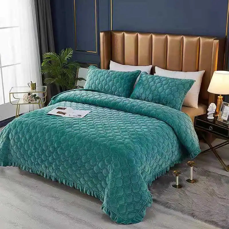 A teal quilted velvet bedspread is draped over a bed with a gold upholstered headboard and dark blue walls.