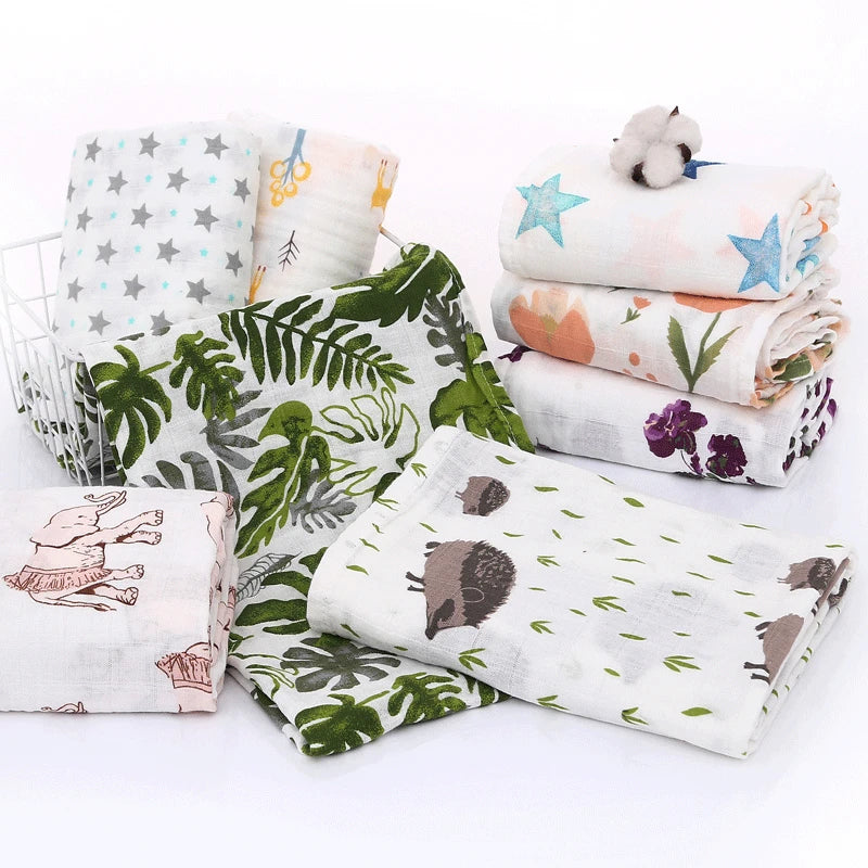 A stack of white cotton muslin swaddle blankets featuring various patterns including stars, leaves, and animals.