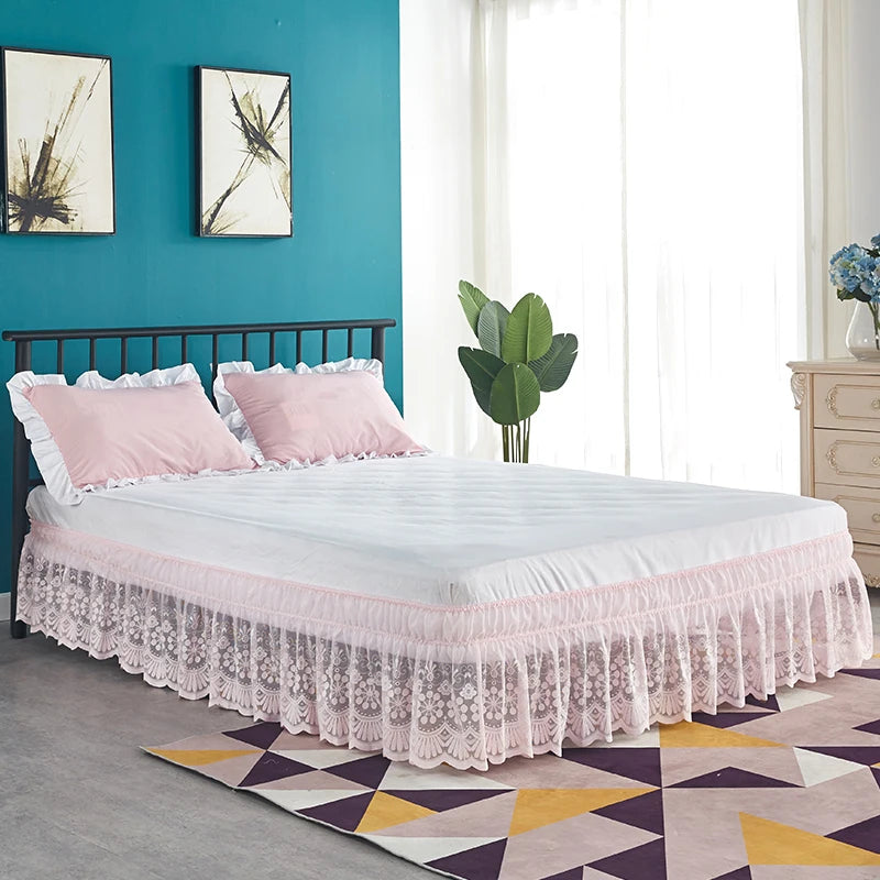 A white bed with a pink lace ruffle skirt and elastic trim in a bright room.
