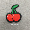 A small embroidered patch of a red cherry with a green stem on a gray background.