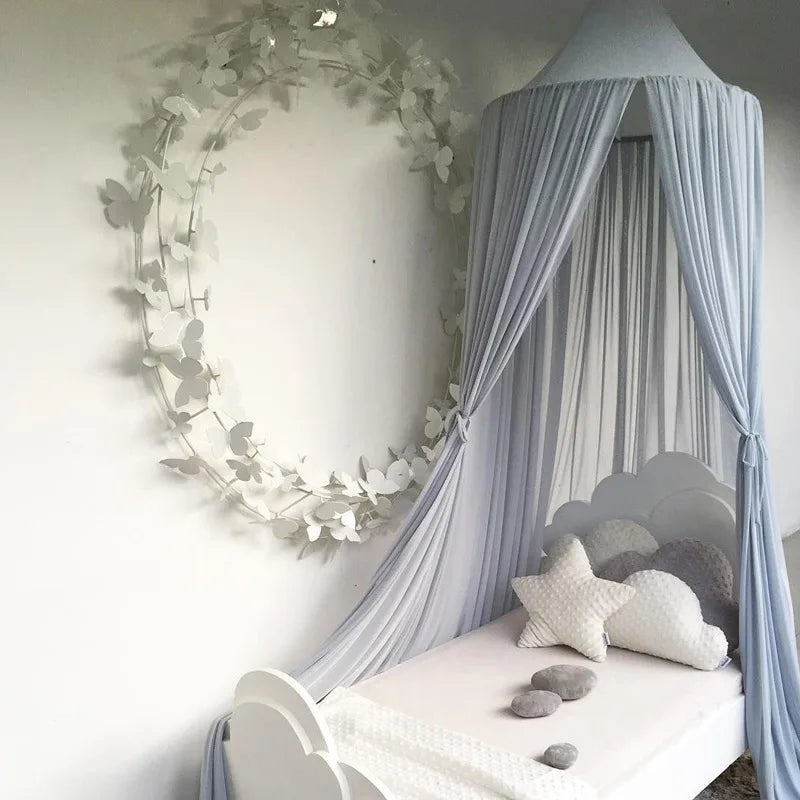 A light blue sheer canopy mosquito net draped over a white bed with soft lighting.